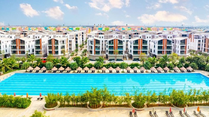 Bể bơi ngoài trời rộng lớn với hàng ghế nghỉ và ô che nắng, phía sau là các tòa nhà căn hộ hiện đại