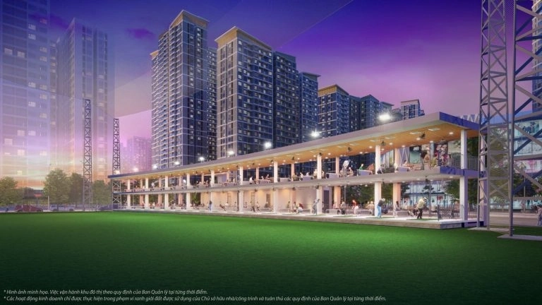 Sân tập golf ngoài trời với nhiều làn đánh, người chơi và các tòa nhà chung cư cao tầng phía sau vào buổi tối.